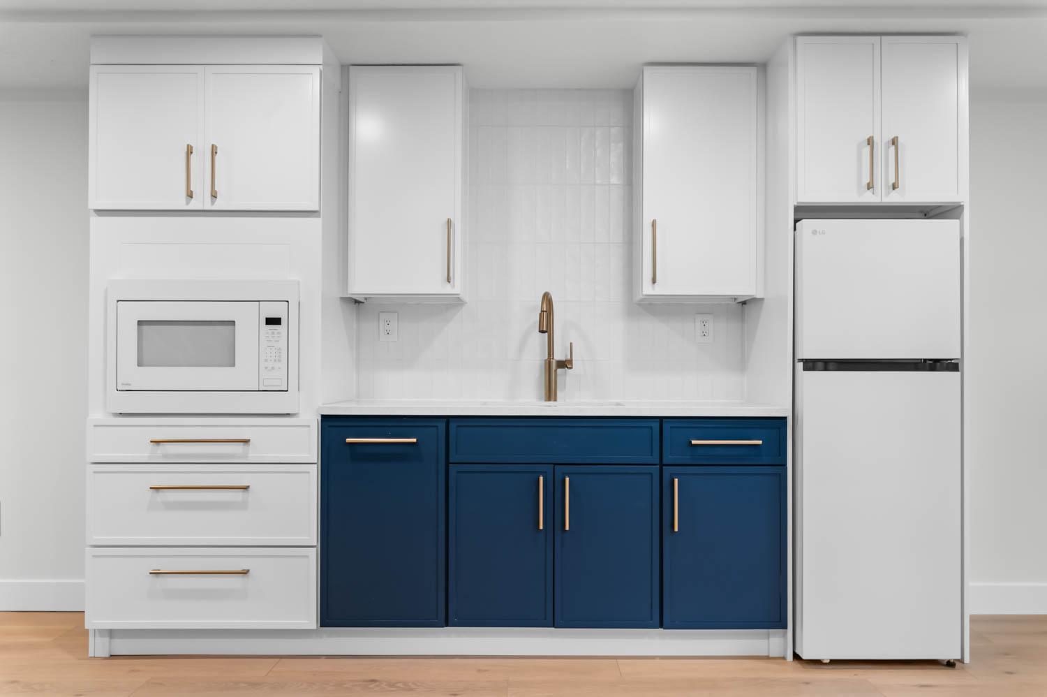 Basement kitchenette remodel with navy shaker cabinets, white uppers, and brass hardware